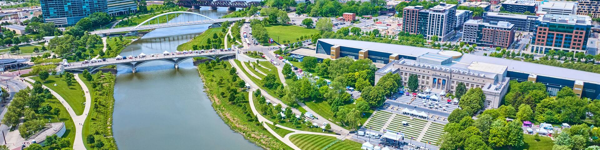A river winding through a city with modern buildings, a bridge, and well-maintained parks.