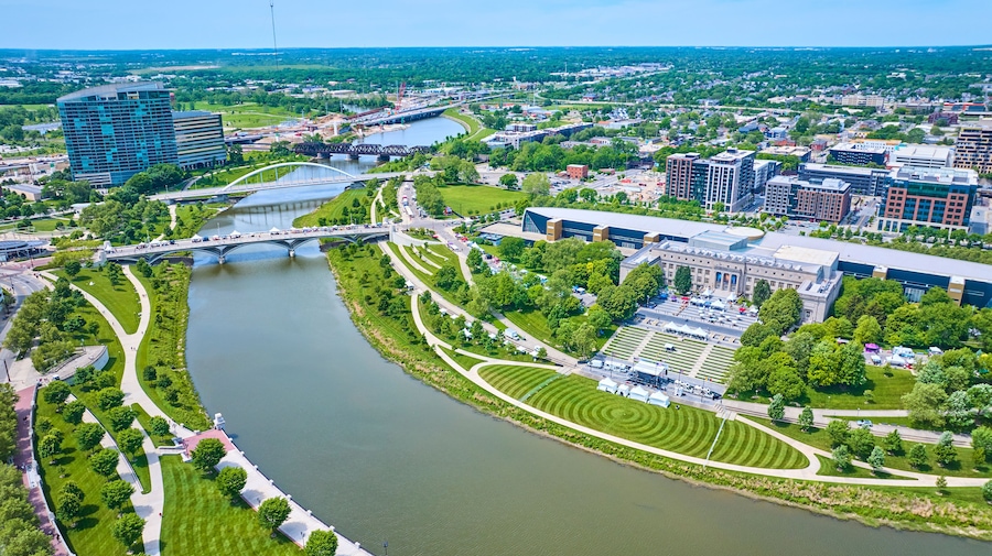 A river winding through a city with modern buildings, a bridge, and well-maintained parks.