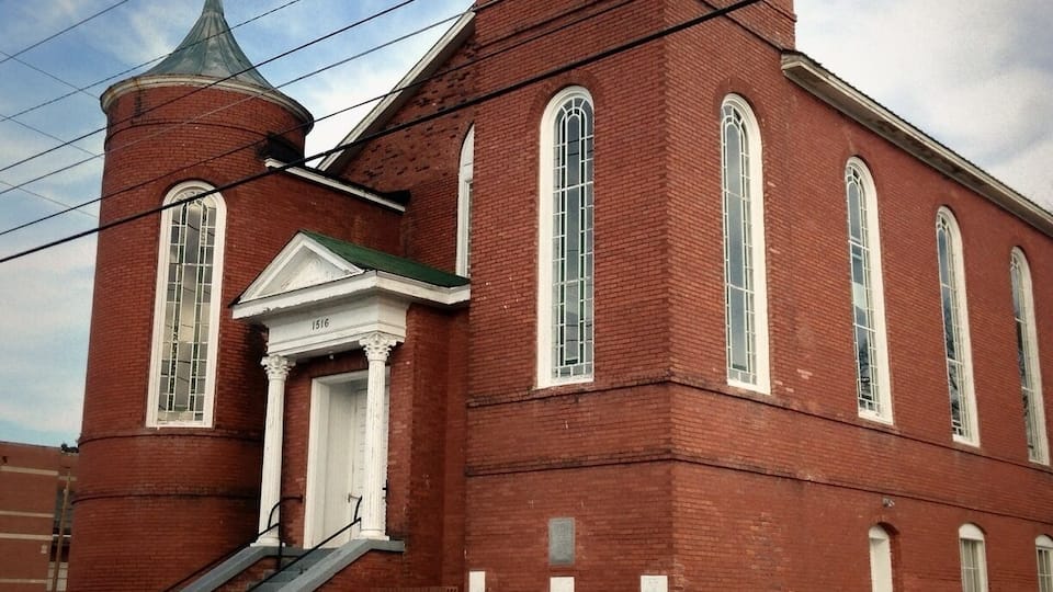 Igreja de tijolos vermelhos com campanário e torre sineira, porta branca e placa de 'For Rent'.