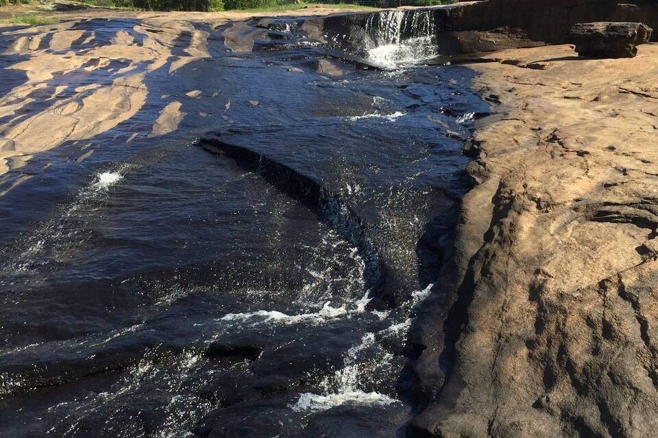 A waterfall cascading over dark rocks surrounded by trees.