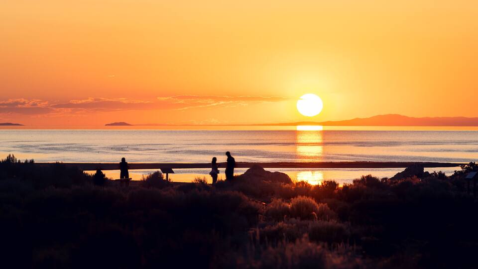 Sun path reflection sunset on Great Salt Lake in Antelope Island State Park with water surface and silhouette of people near campground background
