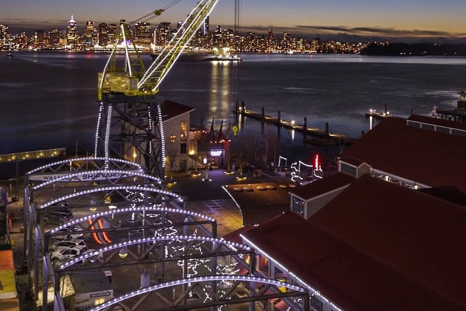 A waterfront with a bridge, illuminated buildings, and a dock.