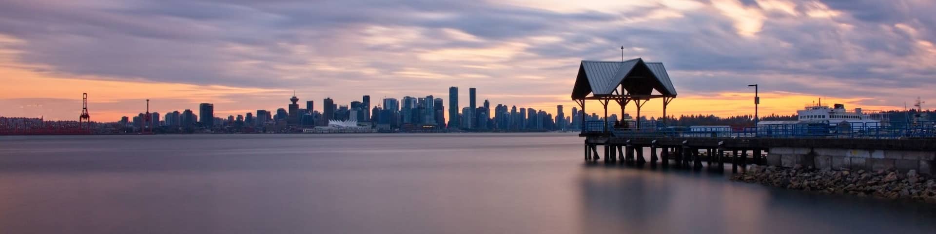 A city skyline at sunset with a pier and a gazebo.