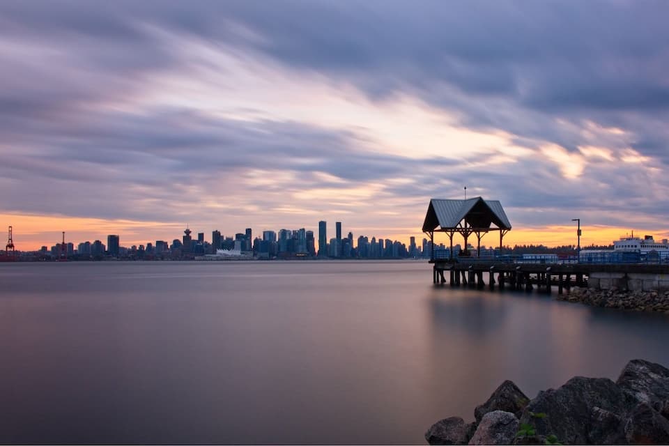 A city skyline at sunset with a pier and a gazebo.