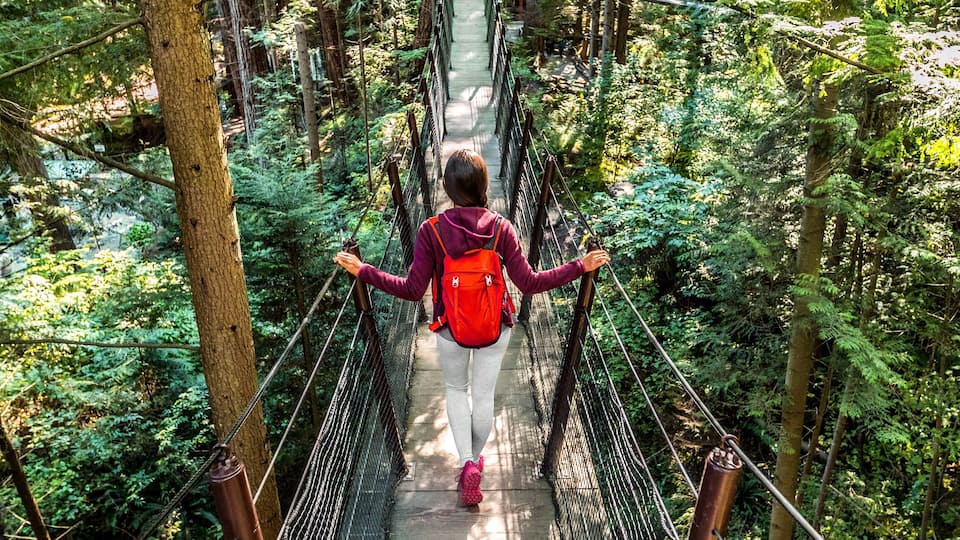 Canada travel people lifestyle banner. Tourist woman walking in famous attraction Capilano Suspension Bridge in North Vancouver, British Columbia, canadian vacation destination for tourism.