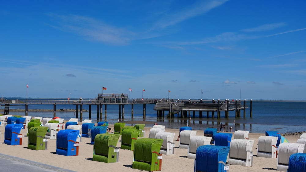 A beach with rows of numbered beach chairs and a pier in the background.