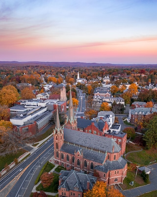 A town with a prominent church, a large industrial building, and autumn-colored trees.