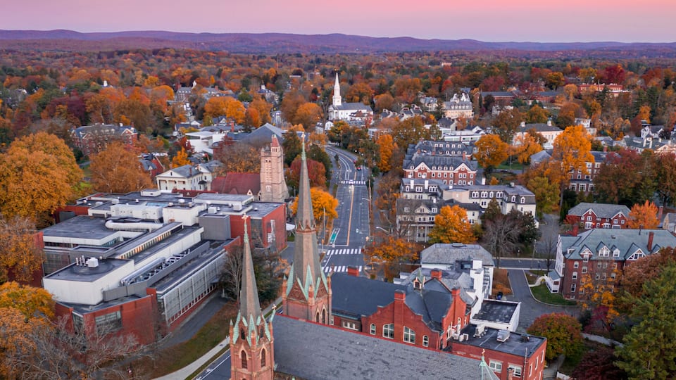 A town with a prominent church, a large industrial building, and autumn-colored trees.