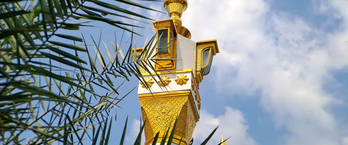 A golden spire with intricate designs against a blue sky with clouds.