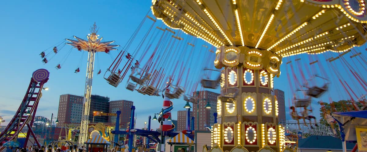 A brightly lit carousel with multiple seats and a Ferris wheel in the background.