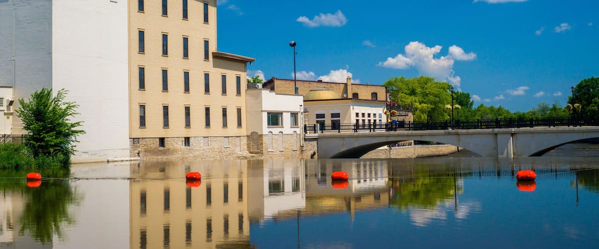 A calm river with reflections of buildings and a bridge.