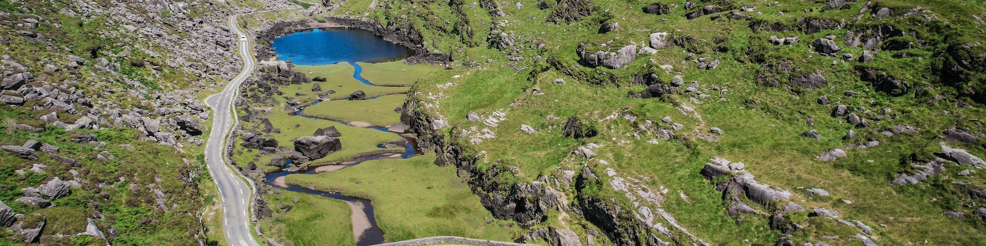 A winding road through a valley with a small lake and rocky terrain.