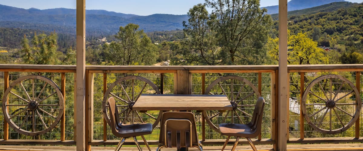 A wooden deck with a table and chairs overlooking a mountainous landscape.