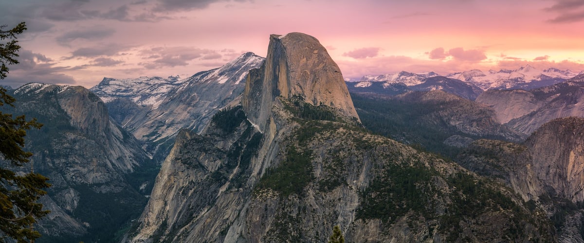 A mountainous landscape with a prominent rock formation, a waterfall, and a forested valley.
