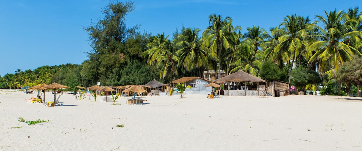 A beach with thatched-roof huts and palm trees.