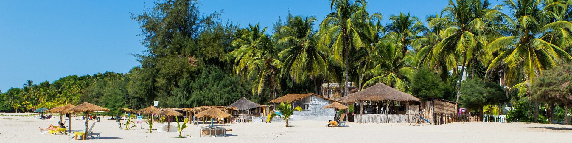 A beach with thatched-roof huts and palm trees.