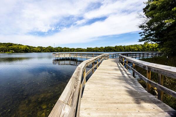 Wooden bridge over the reflective clean lake Carver surrounded by dense trees in Minnesota