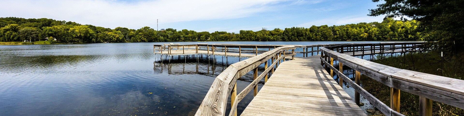 Wooden bridge over the reflective clean lake Carver surrounded by dense trees in Minnesota