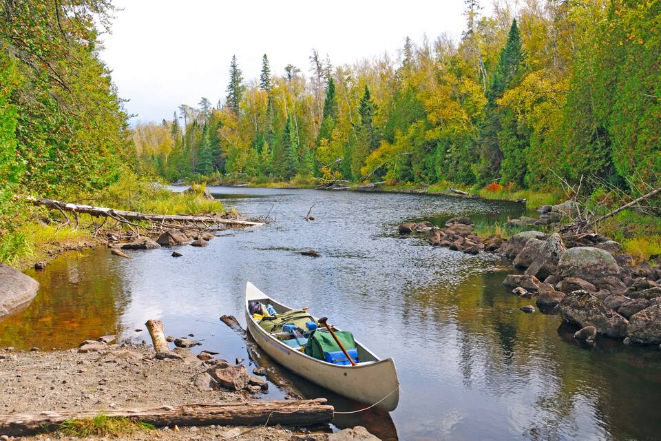 Un canoë était amarré sur une rive rocheuse, avec le feuillage automnal en arrière-plan.