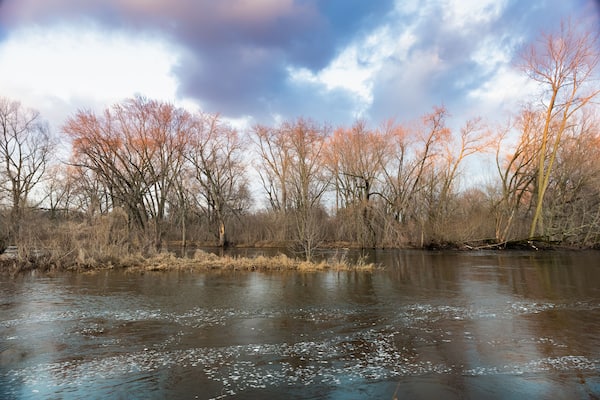 River banks in early spring. Clouds reflecting in moving water of stream.
