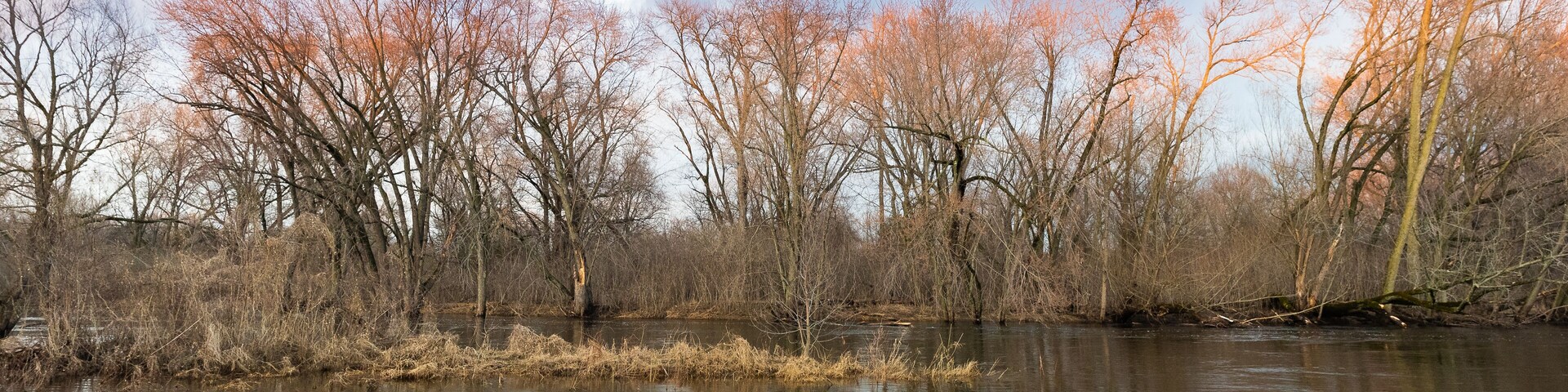 River banks in early spring. Clouds reflecting in moving water of stream.