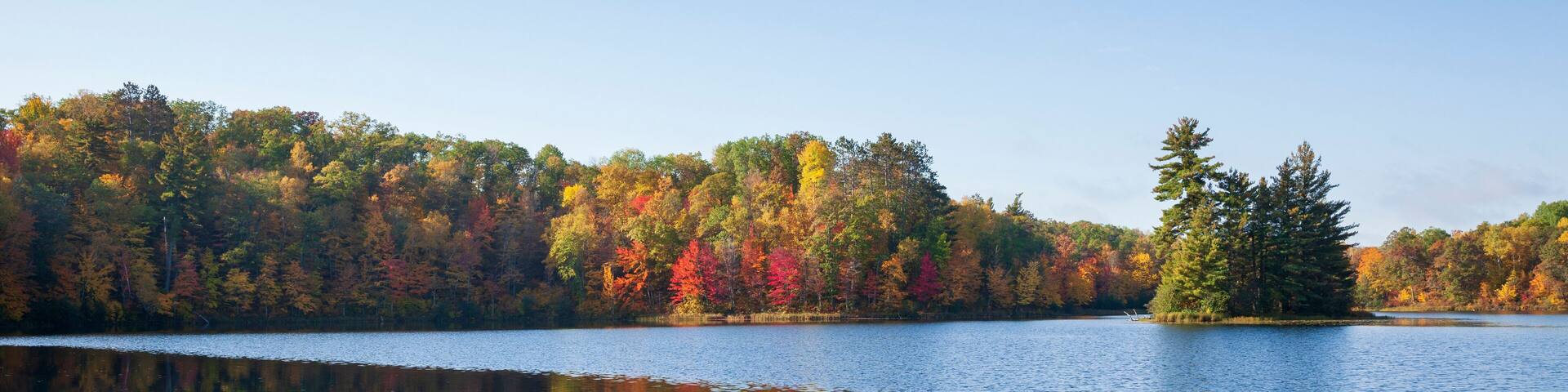 Un lac paisible où se reflètent les arbres aux couleurs vives de l’automne.