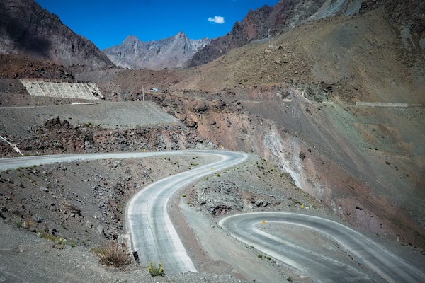 A winding mountain road with rocky terrain and distant mountains.