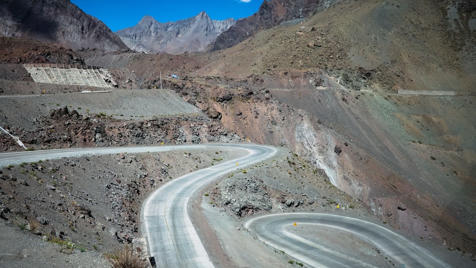 A winding mountain road with rocky terrain and distant mountains.