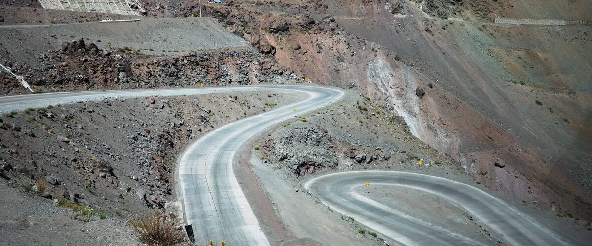 A winding mountain road with rocky terrain and distant mountains.