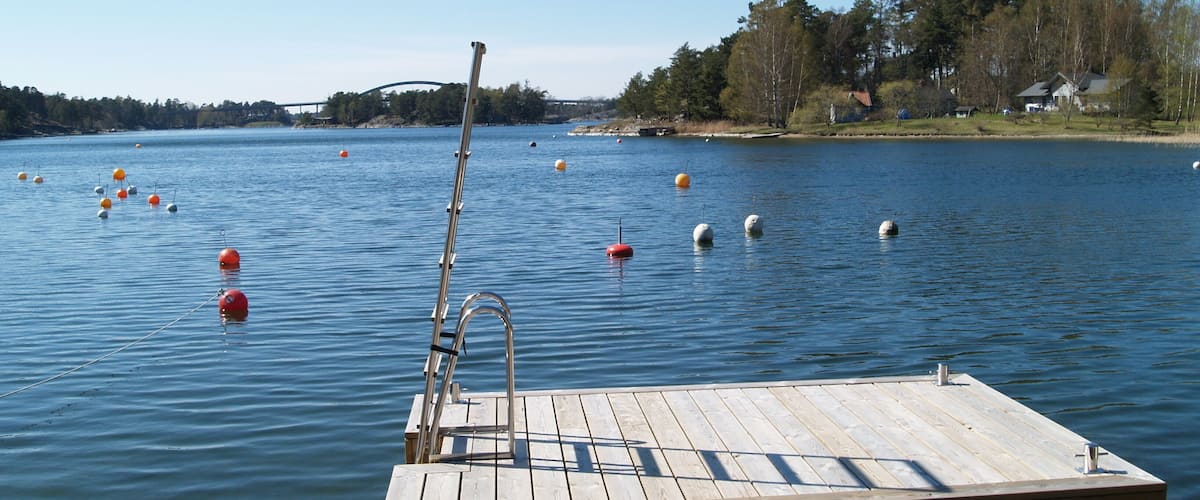 A wooden dock extending into a calm lake with buoys and a distant bridge.