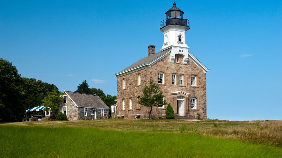 A historic stone building with a lighthouse on top, a smaller adjacent structure, and a grassy field in the foreground.