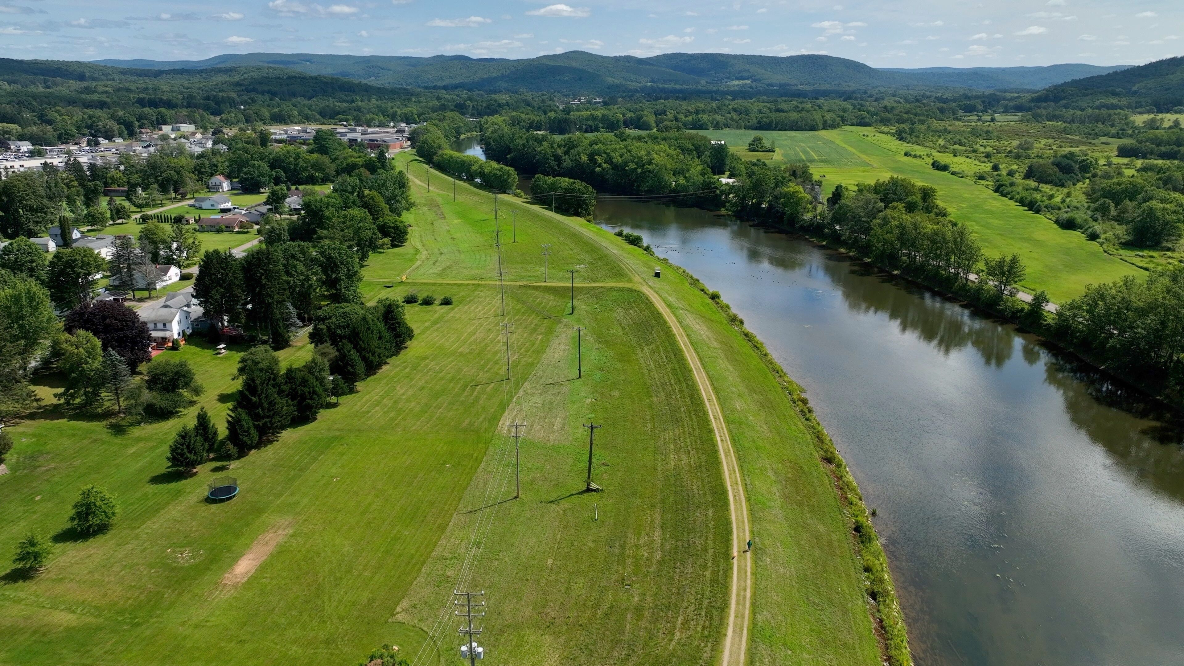Peaceful countryside landscape in Olean, NY with river, hills, green pastures under blue sky and clouds