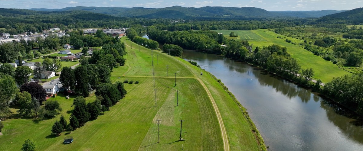 Peaceful countryside landscape in Olean, NY with river, hills, green pastures under blue sky and clouds