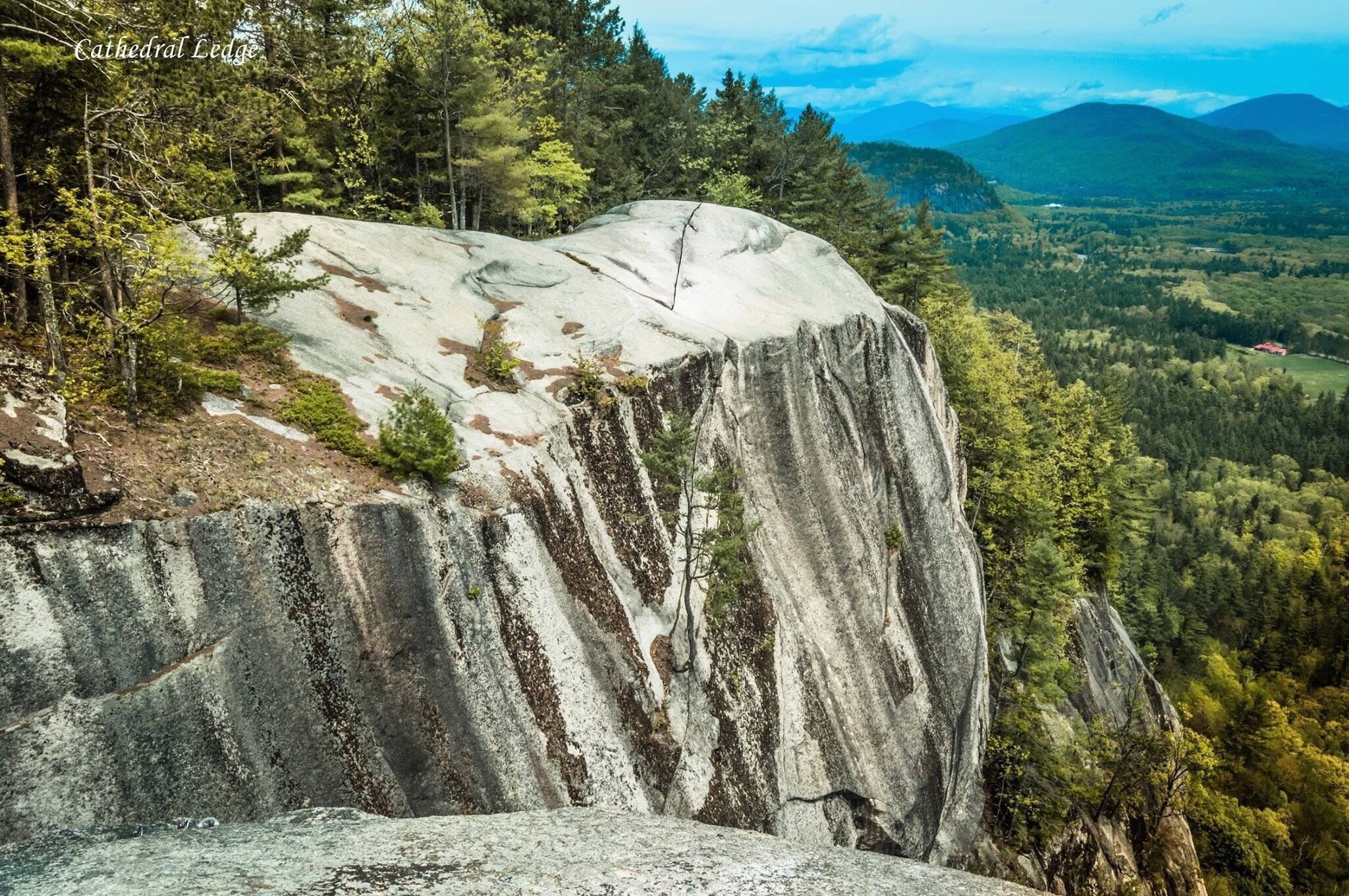 A large rock formation with a forested valley in the background.
