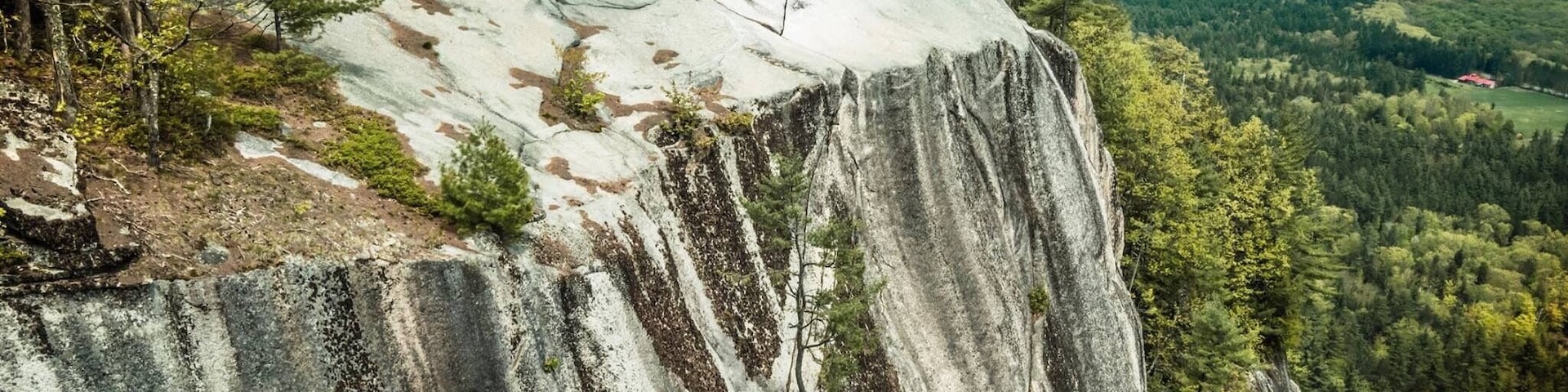 Uma grande formação rochosa com um vale arborizado ao fundo.
