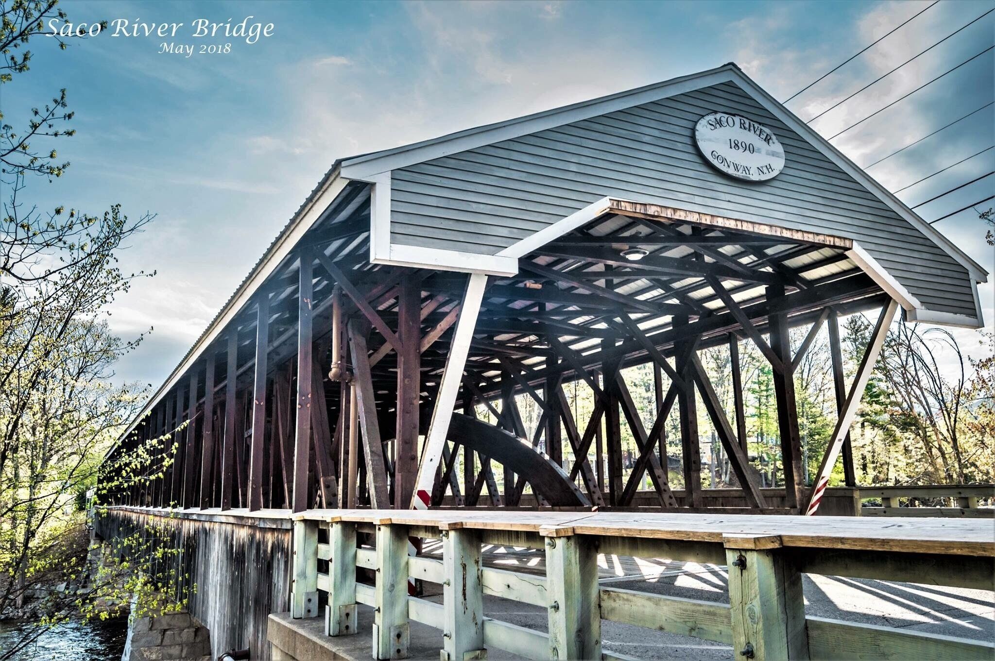 A covered wooden bridge with a sign reading "Saco River Bridge 1890 GONWAY, NH."