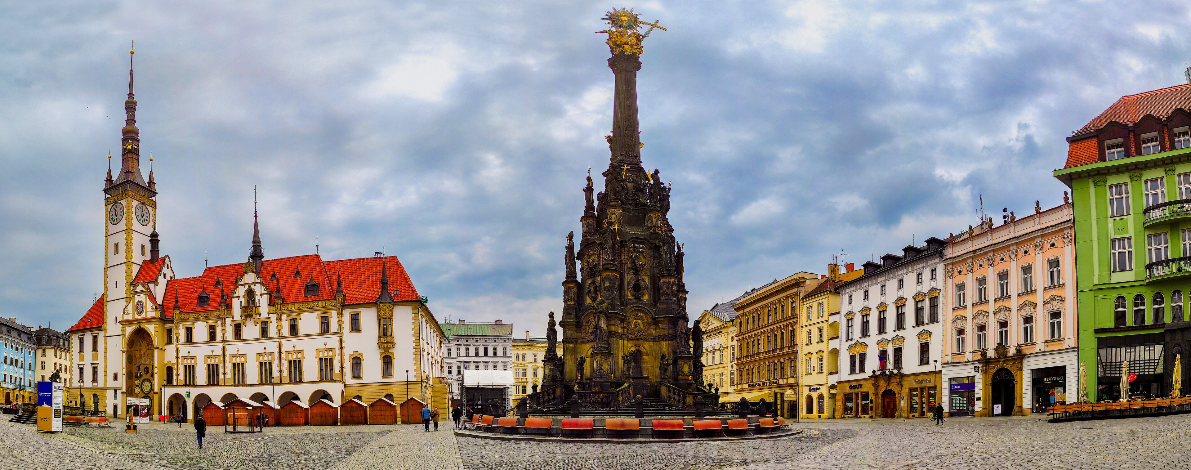 Una plaza histórica con una torre alta, un monumento central y edificios coloridos a su alrededor.