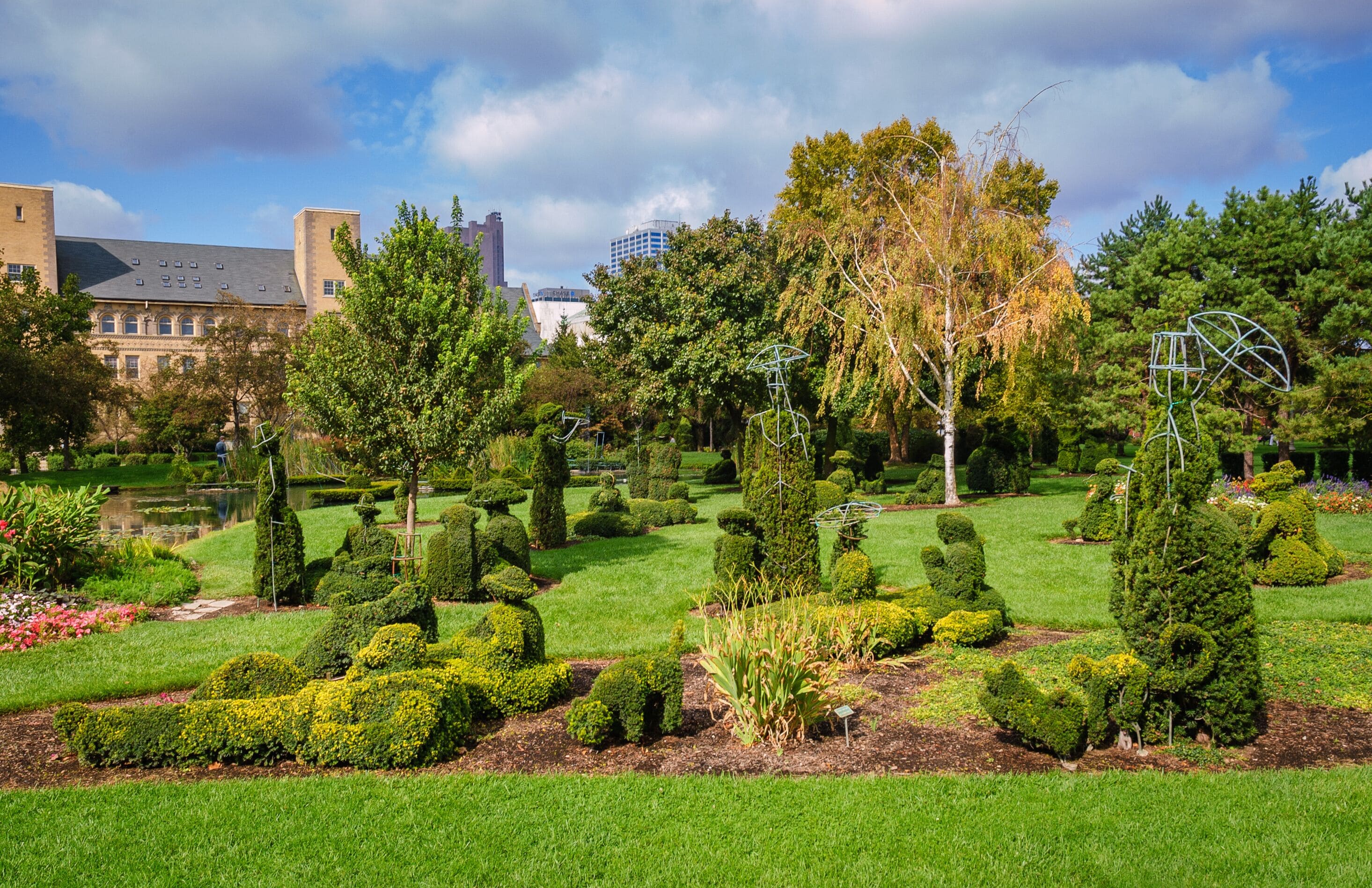 A well-manicured garden with topiary, a pond, and a variety of trees and shrubs.