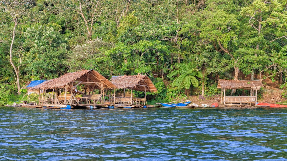 Floating houses on a river surrounded by dense forest.