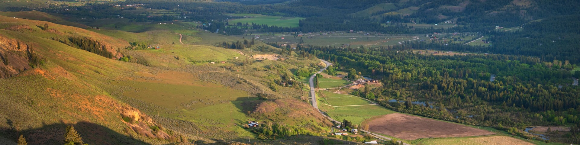 A mountainous landscape with a winding road, green fields, and scattered buildings.