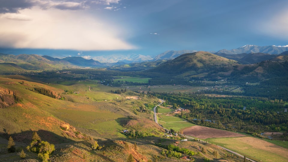 A mountainous landscape with a winding road, green fields, and scattered buildings.