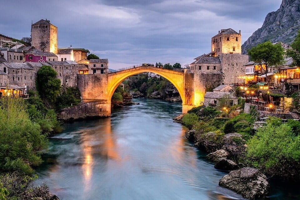A stone bridge over a river, surrounded by historic buildings and greenery.