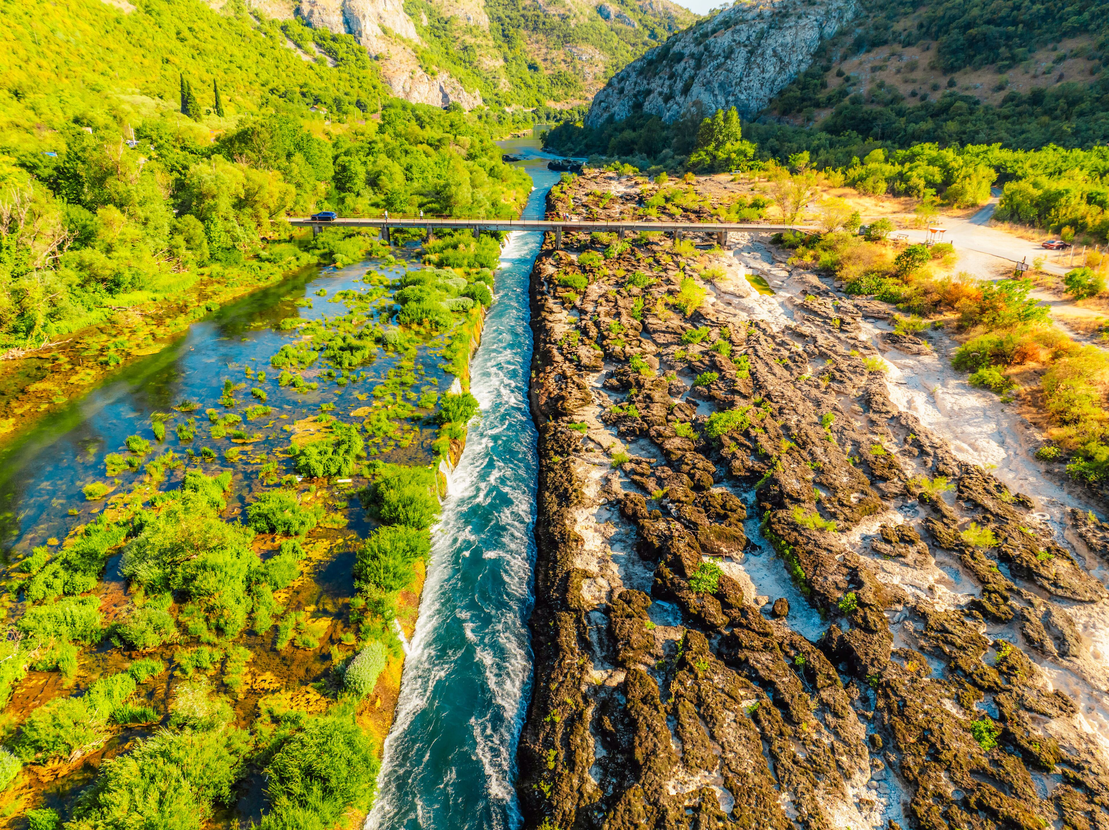 Um rio com margens rochosas, uma ponte e uma paisagem montanhosa.