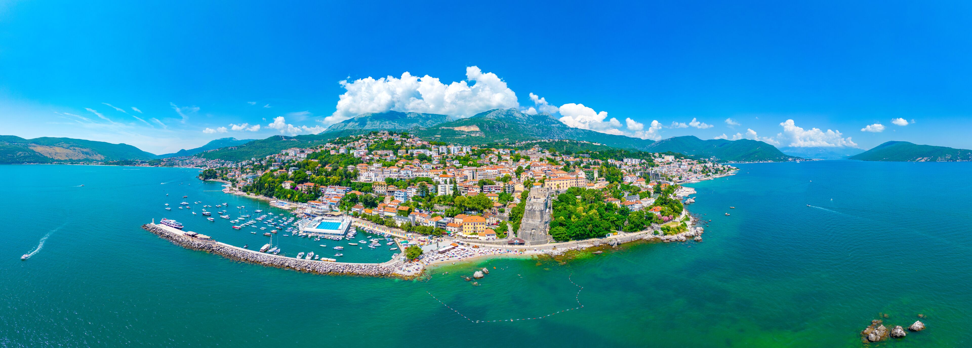 A coastal town with a marina, historic buildings, and a mountainous backdrop.