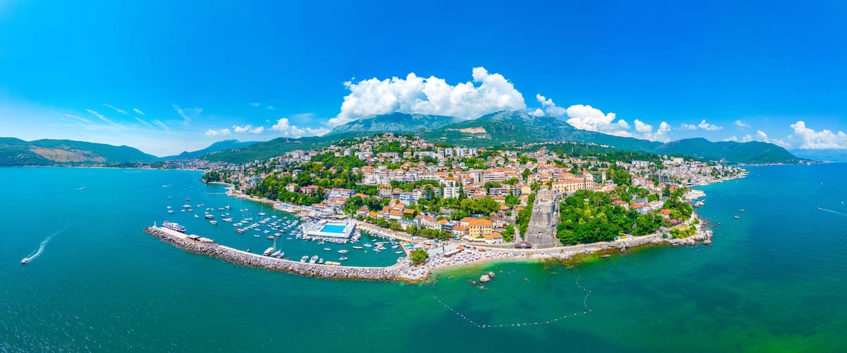 A coastal town with a marina, historic buildings, and a mountainous backdrop.