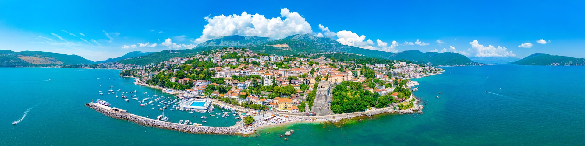 A coastal town with a marina, historic buildings, and a mountainous backdrop.