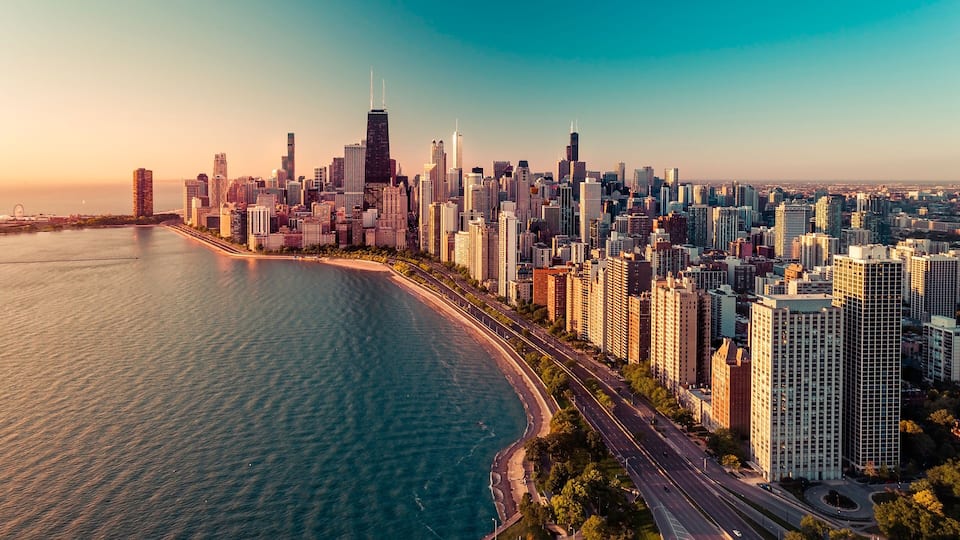 A coastal cityscape with a prominent skyscraper, a curved waterfront, and a dense cluster of high-rise buildings.