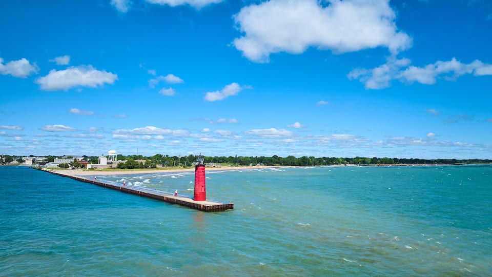 A coastal scene with a red lighthouse, clear blue sky, and calm sea.
