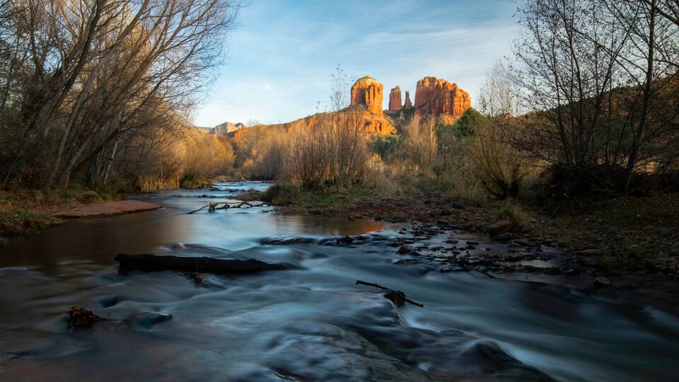A river flowing through a forest with a rocky outcrop in the background.