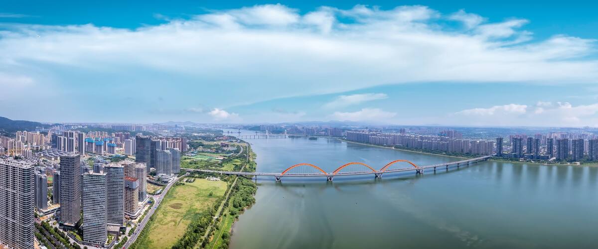 A river with a bridge, a cityscape with high-rise buildings, and a clear blue sky.
